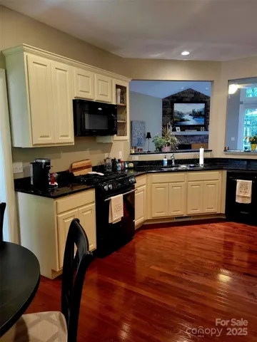 a kitchen with stainless steel appliances granite countertop a stove top oven a sink dishwasher and white cabinets with wooden floor