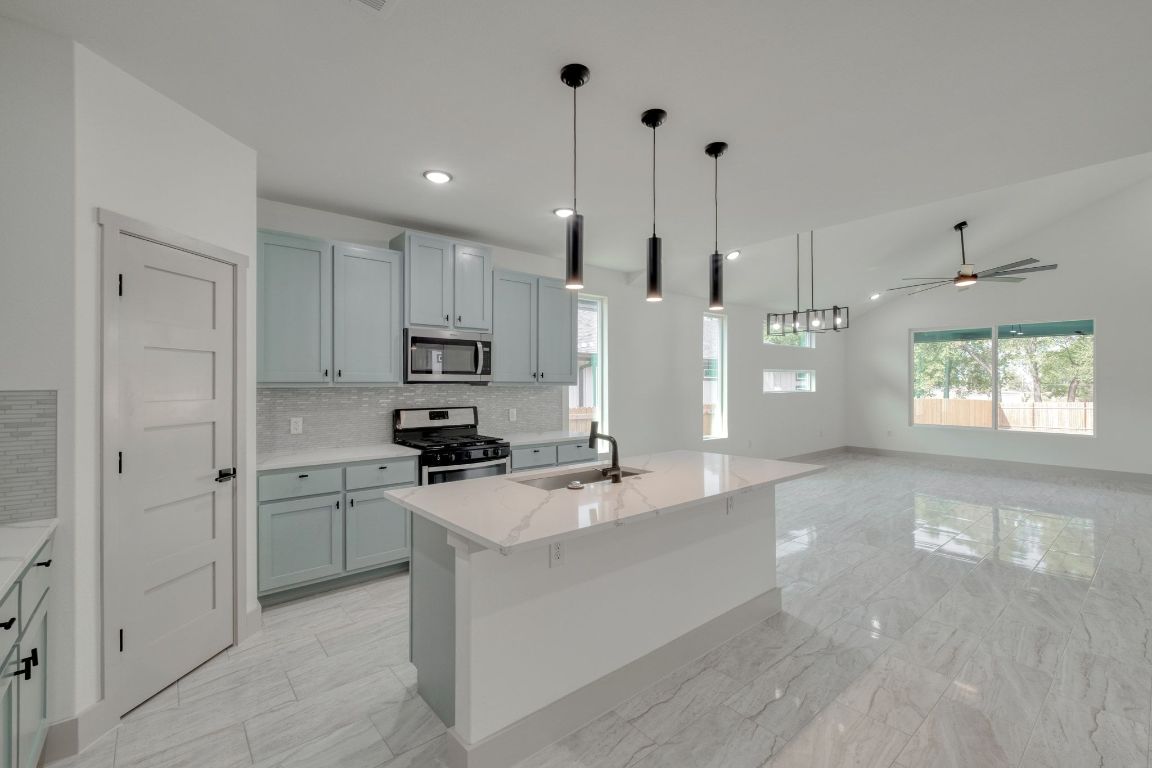 202 Washington Street Elgin, TX 78621 - Photo 5 of 26 Kitchen with decorative backsplash, pendant lighting, light stone counters, appliances with stainless steel finishes, and a kitchen island you can sit at with sink