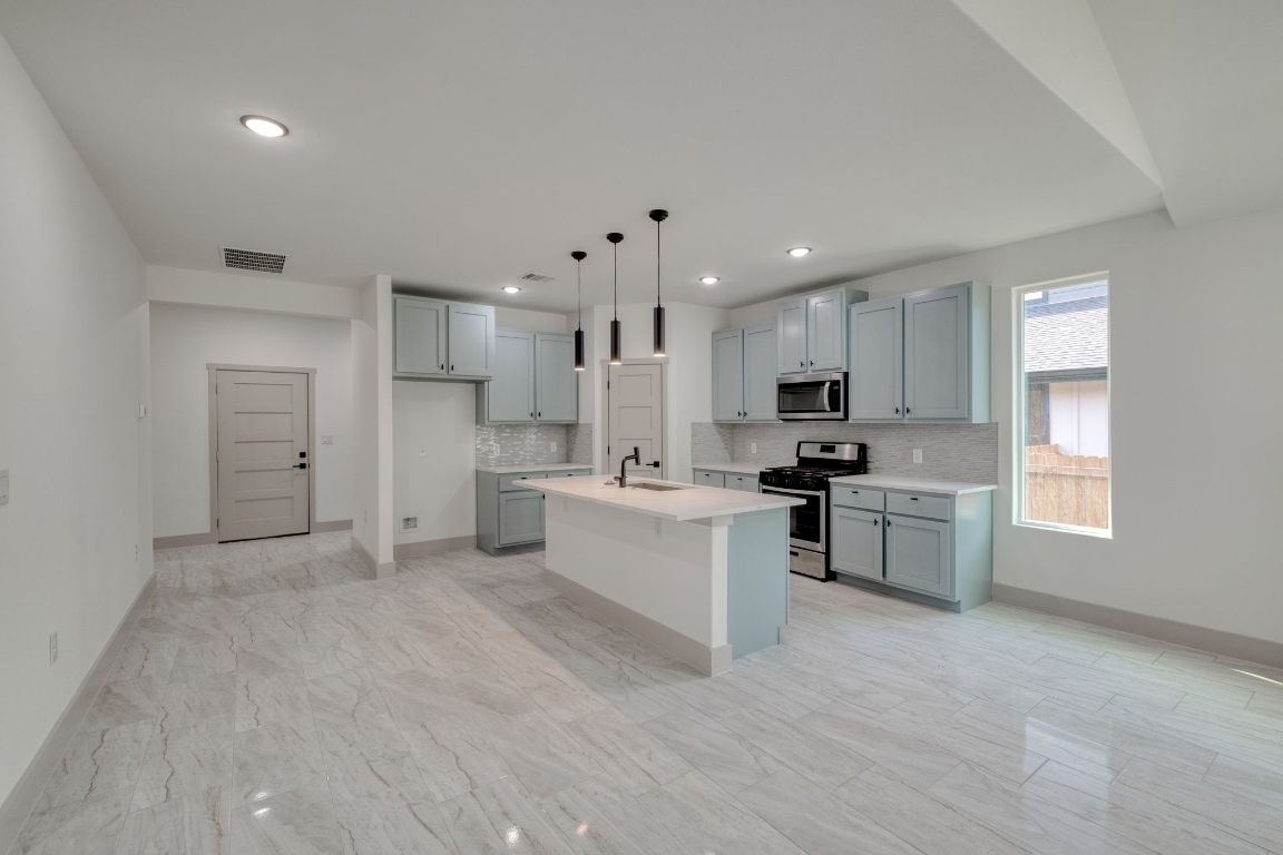 202 Washington Street Elgin, TX 78621 - Photo 6 of 26 Kitchen with a kitchen breakfast bar, backsplash, appliances with stainless steel finishes, a center island with seating and sink, and pendant lighting