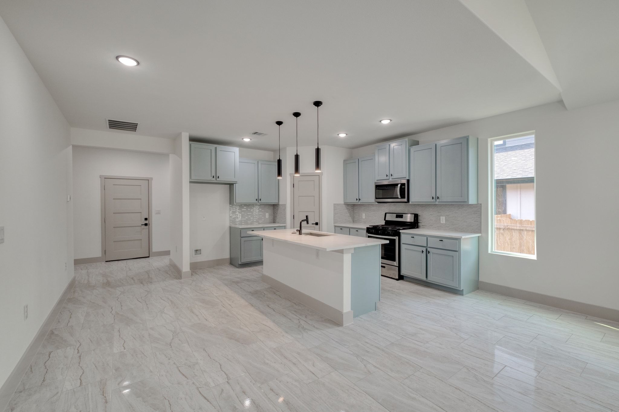 202 Washington Street Elgin, TX 78621 - Photo 6 of 26 Kitchen with a kitchen breakfast bar, backsplash, appliances with stainless steel finishes, a center island with seating and sink, and pendant lighting
