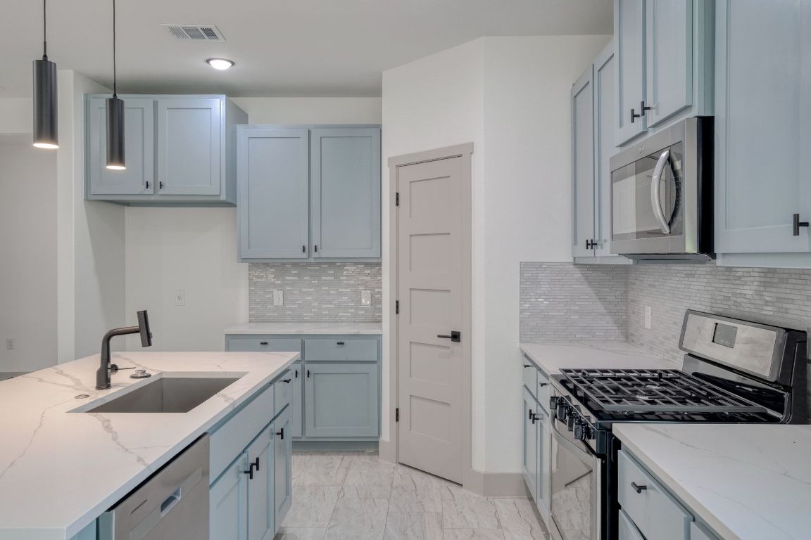 202 Washington Street Elgin, TX 78621 - Photo 7 of 26 Kitchen with stainless steel appliances, hanging light fixtures, light stone countertops, an island with sink, and recessed lighting