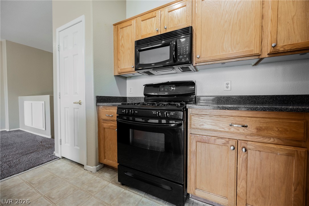 6320 Snap Ridge Street, Unit 201 North Las Vegas, NV 89081 - Photo 24 of 56 A compact kitchen featuring warm wooden cabinetry and essential cooking appliances.