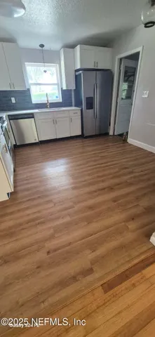 a view of an empty room with kitchen and window