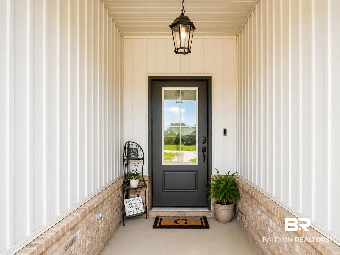 1097 Stella Road Foley, AL 36535 - Photo 5 of 15 Front entry featuring a dark-paneled door with an integrated window, board and batten siding, brick wainscoting, a concrete porch, and an overhead lantern-style light fixture