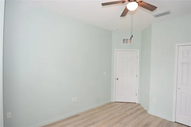 an empty room with a chandelier fan and wooden floor