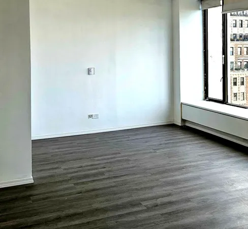 a view of an empty room with wooden floor and a window