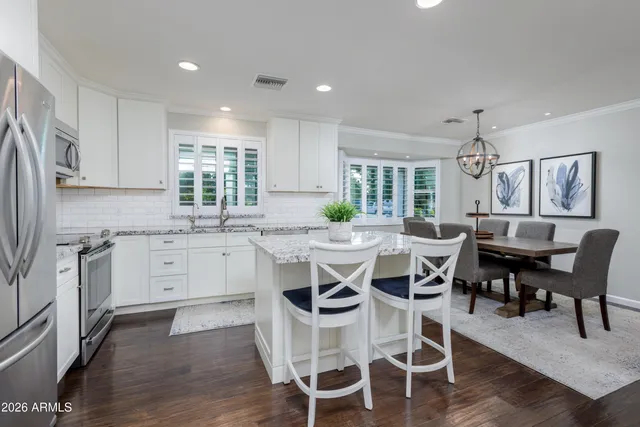 a kitchen with a dining table chairs wooden floor cabinets appliances and a window