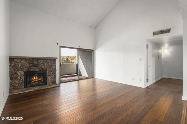 a view of an empty room with wooden floor fireplace and a window