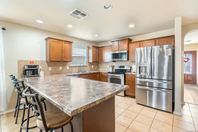 a kitchen with stainless steel appliances granite countertop a refrigerator a stove a sink a dining table and chairs