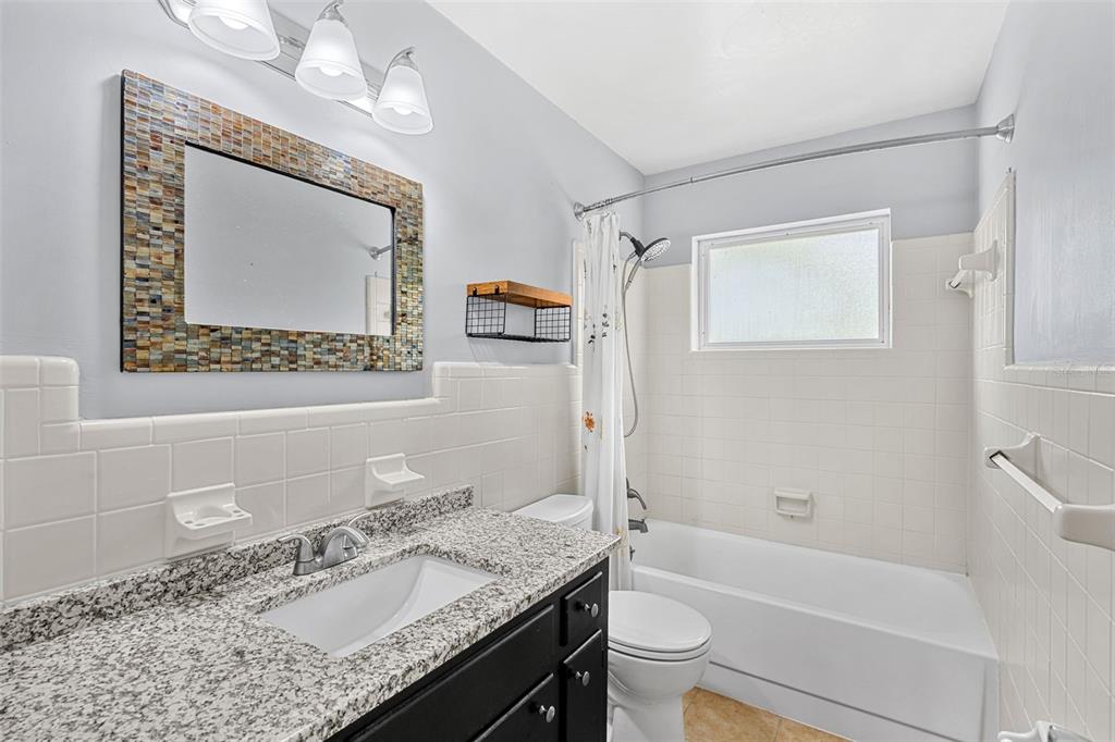 2923 Conway Gardens Road Orlando, FL 32806 - Photo 11 of 28 a bathroom with a granite countertop sink a mirror a toilet a bathtub and shower