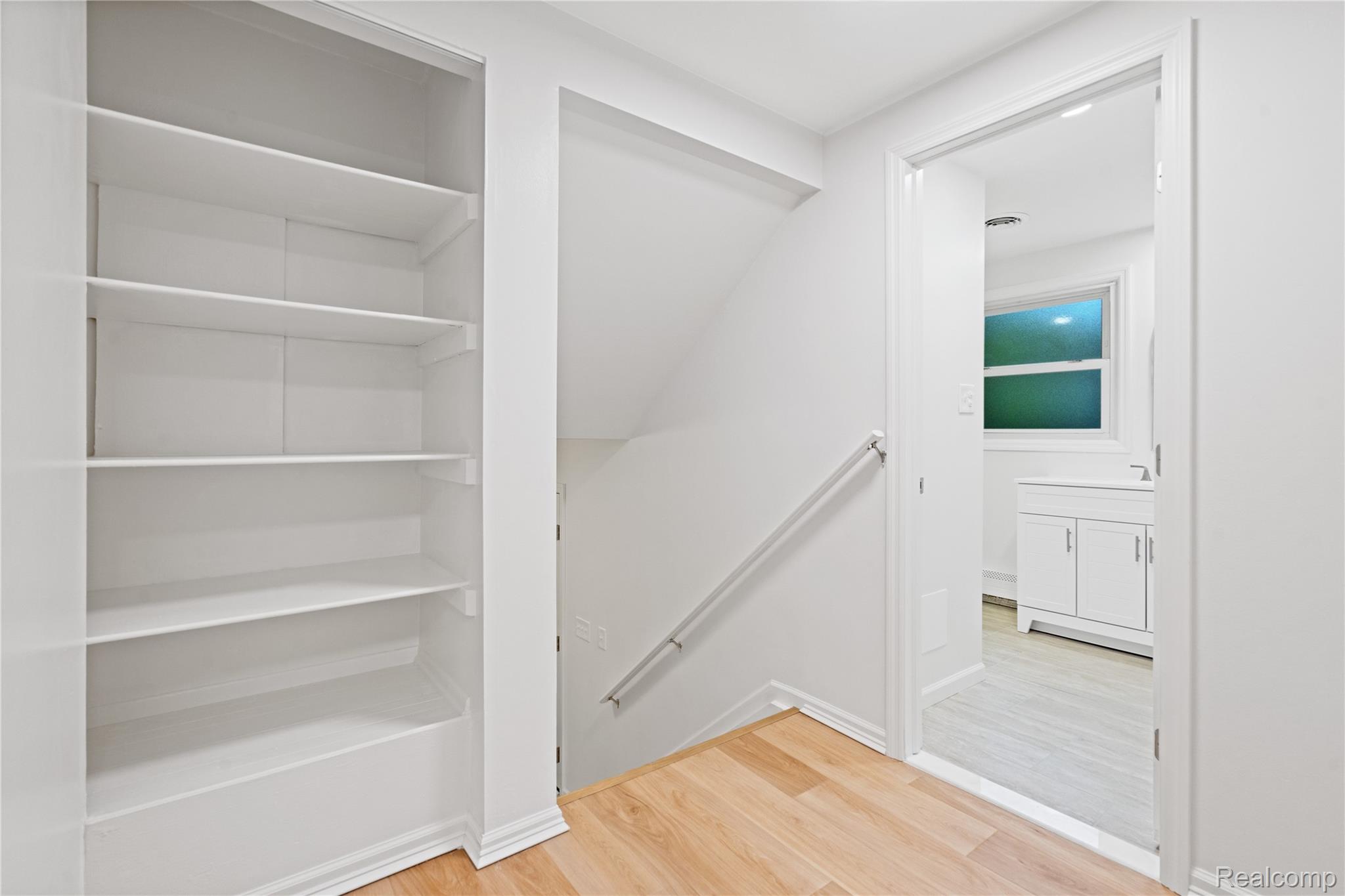 8240 Hampton Road Grosse Ile, MI 48138 - Photo 13 of 33 Built-in shelving, wood-finish flooring, white wall paint, handrail, and a doorway leading to a room with a window and white vanity