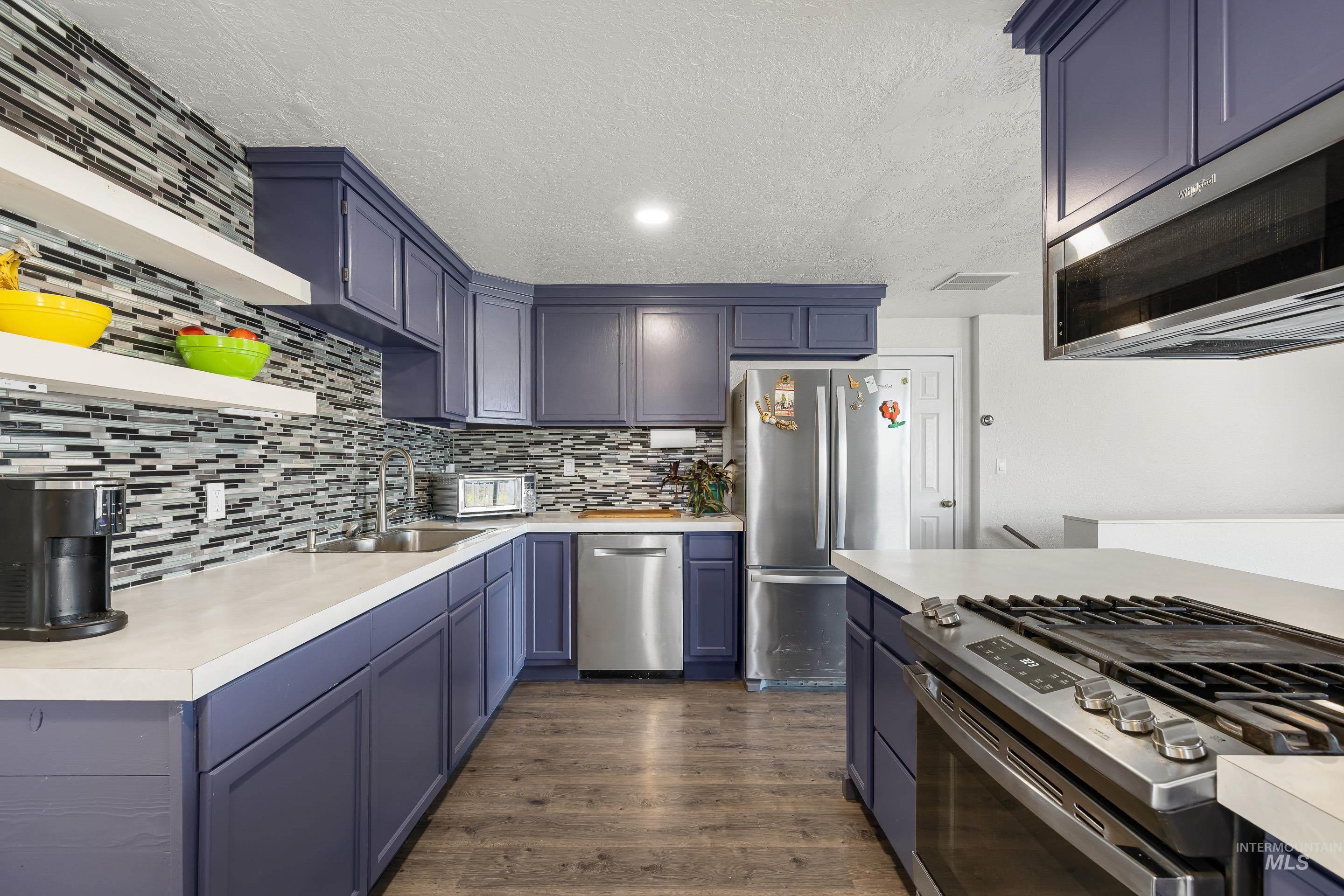 Kitchen featuring light countertops, stainless steel appliances, dark wood finished floors, blue cabinets, and tasteful backsplash
