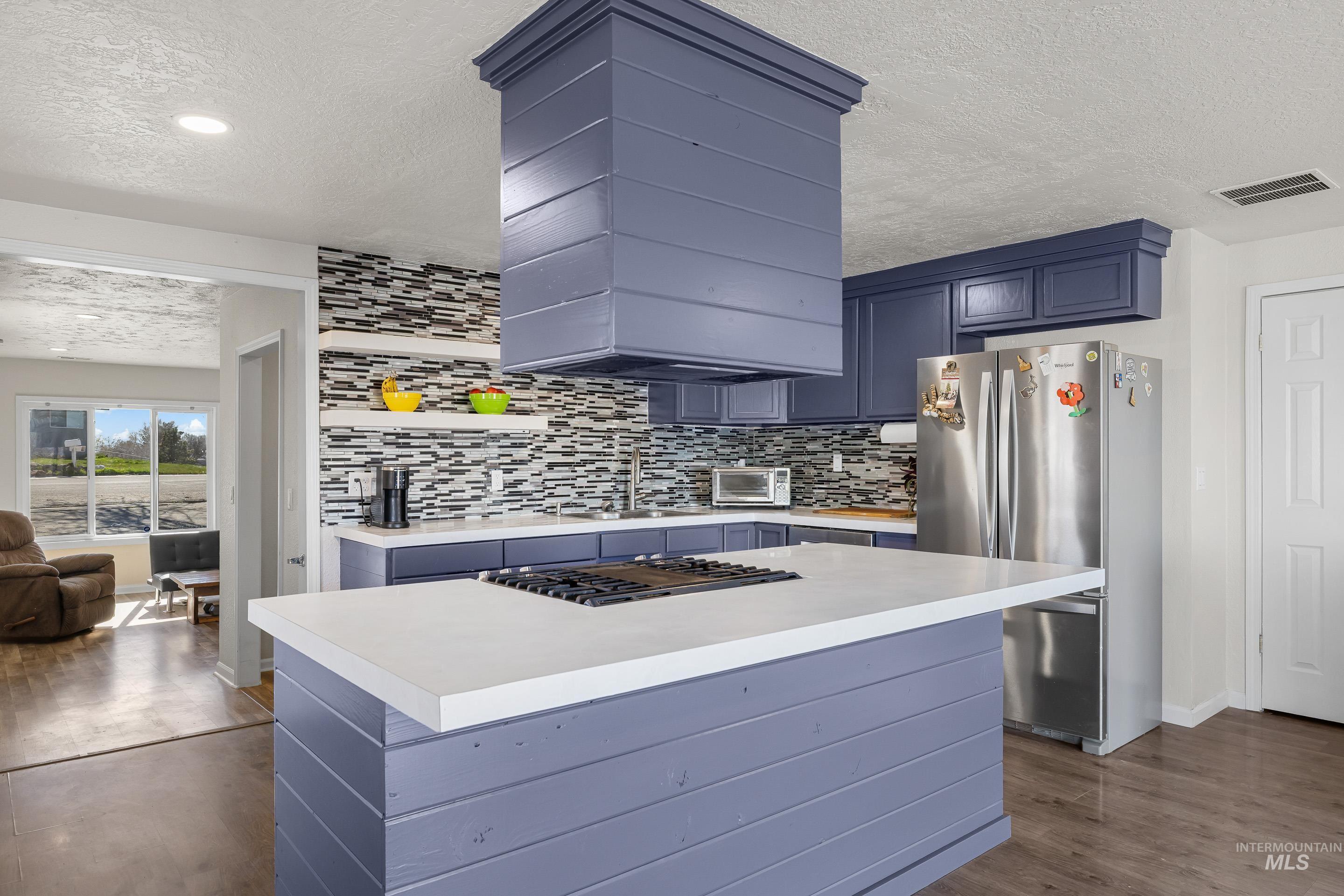 10294 West Fox Ridge Drive Boise, ID 83709 - Photo 10 of 50 Kitchen with light countertops, freestanding refrigerator, a textured ceiling, a center island, and backsplash