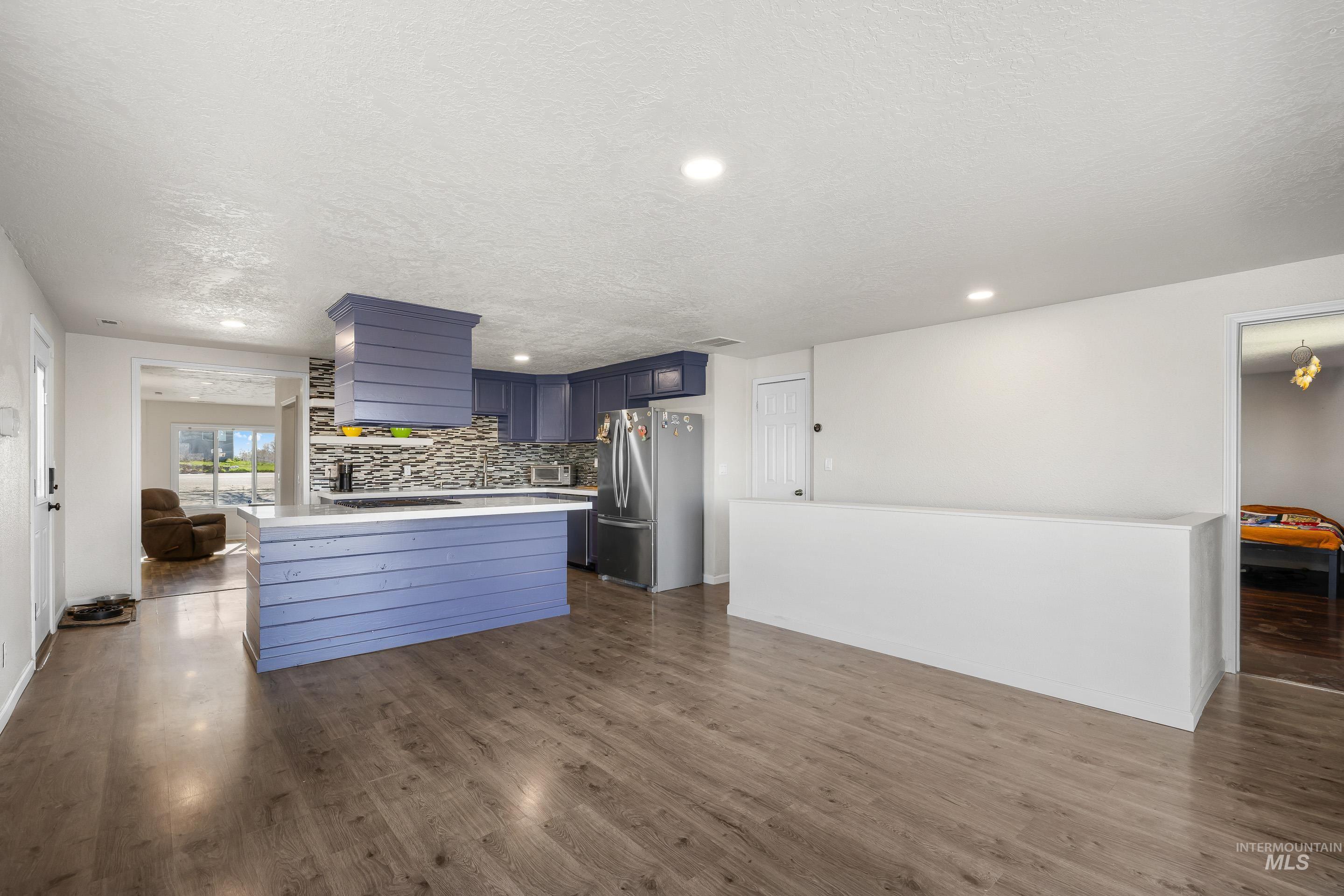 10294 West Fox Ridge Drive Boise, ID 83709 - Photo 50 of 50 Kitchen featuring blue cabinets, stainless steel appliances, a textured ceiling, decorative backsplash, and open floor plan