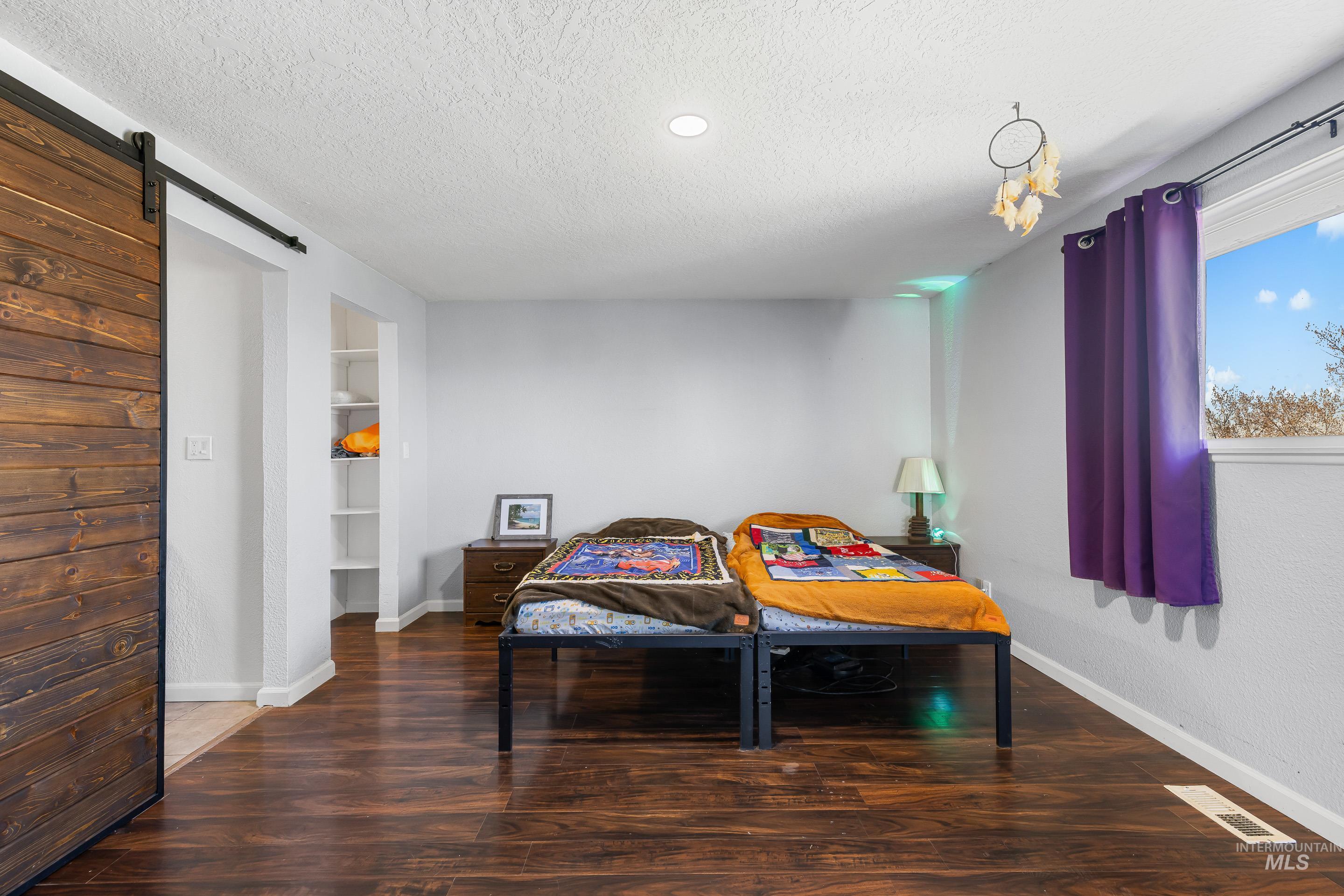 10294 West Fox Ridge Drive Boise, ID 83709 - Photo 16 of 50 Bedroom featuring a barn door, dark wood-type flooring, and a textured ceiling
