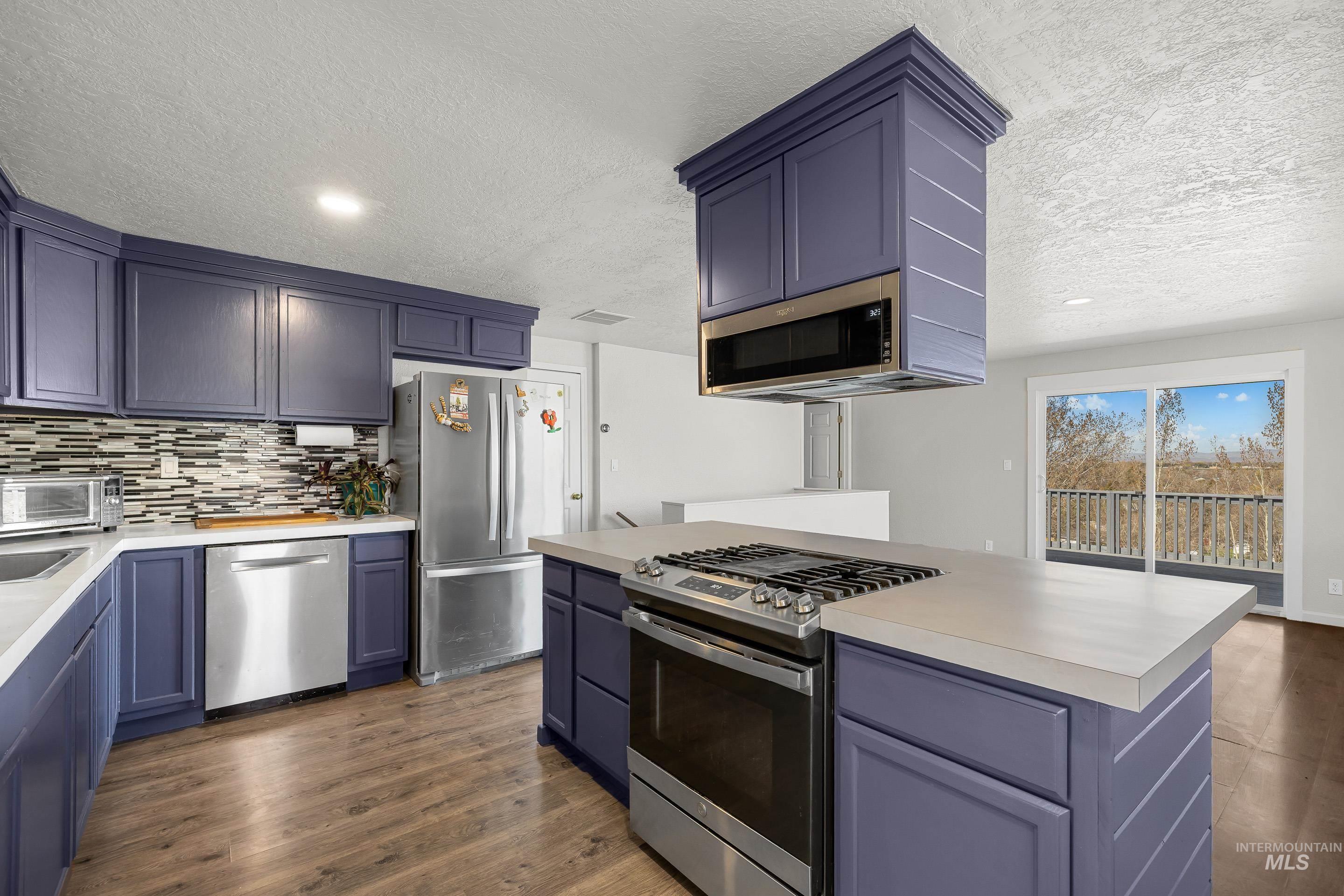 10294 West Fox Ridge Drive Boise, ID 83709 - Photo 8 of 50 Kitchen with stainless steel appliances, light countertops, dark wood-type flooring, decorative backsplash, and a textured ceiling