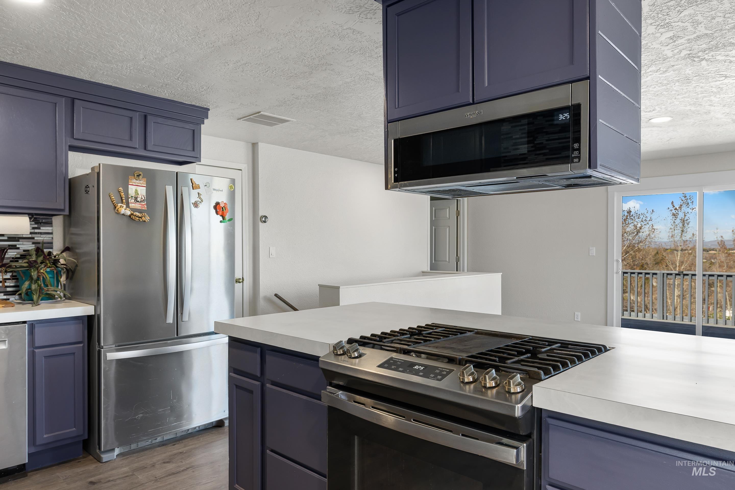10294 West Fox Ridge Drive Boise, ID 83709 - Photo 9 of 50 Kitchen featuring light countertops, stainless steel appliances, a textured ceiling, dark wood-style floors, and tasteful backsplash