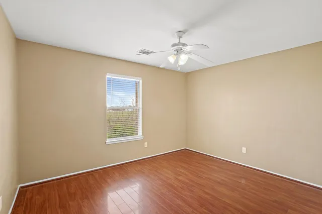 an empty room with wooden floor chandelier fan and windows