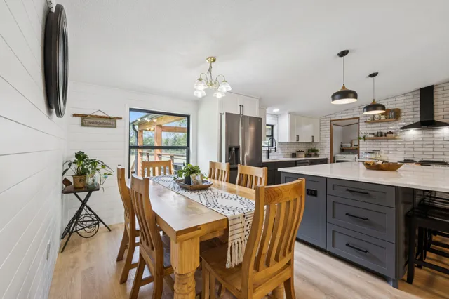 a kitchen with stainless steel appliances kitchen island granite countertop a stove a refrigerator a dining table and chairs with wooden floor