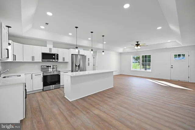 a large white kitchen with stainless steel appliances granite countertop a stove a sink a refrigerator white cabinets and wooden floor