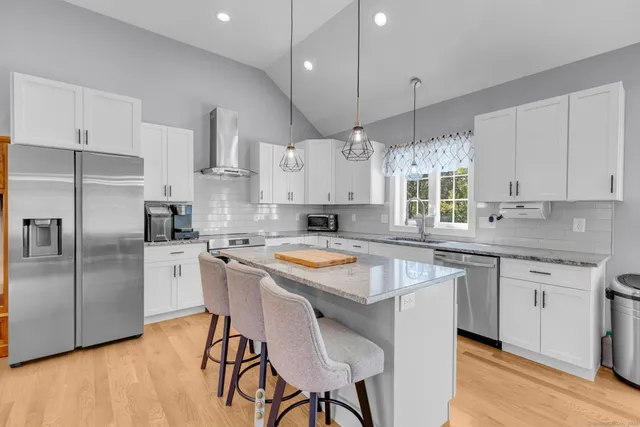 a kitchen with stainless steel appliances granite countertop a stove a sink a microwave a refrigerator and white cabinets with wooden floor