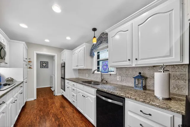 a kitchen with granite countertop a sink dishwasher stove and white cabinets with wooden floor