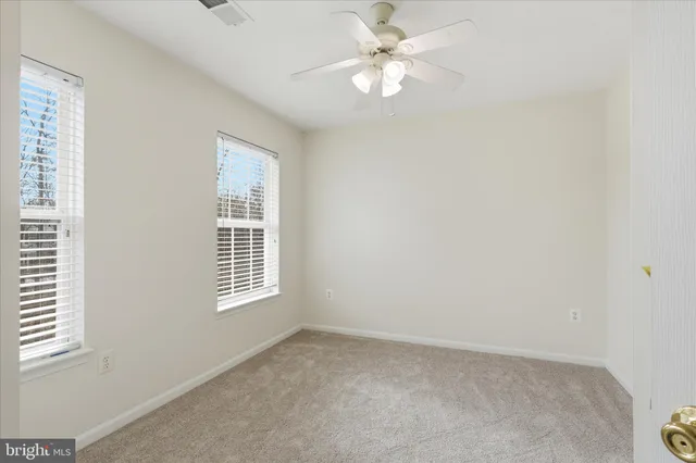an empty room with chandelier fan and windows