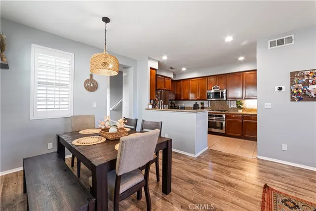 a kitchen with stainless steel appliances kitchen island granite countertop a stove a sink a refrigerator and a dining table with wooden floor