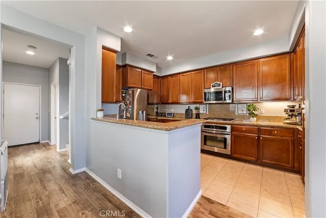 a kitchen with stainless steel appliances granite countertop a refrigerator a sink dishwasher a stove with wooden cabinets and floor