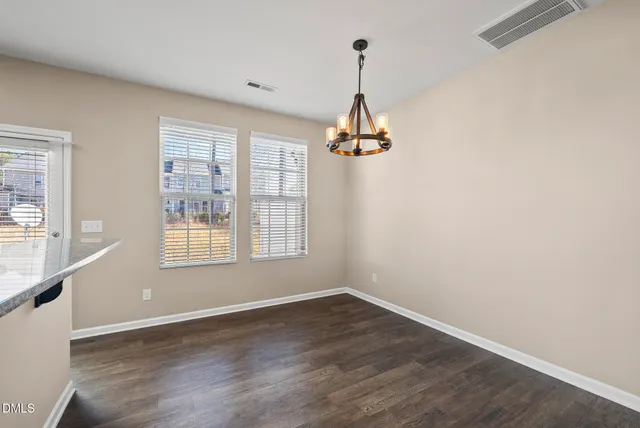 a view of an empty room with wooden floor and a kitchen