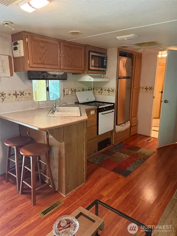 a kitchen with stainless steel appliances granite countertop a refrigerator a stove a sink and white cabinets with wooden floor