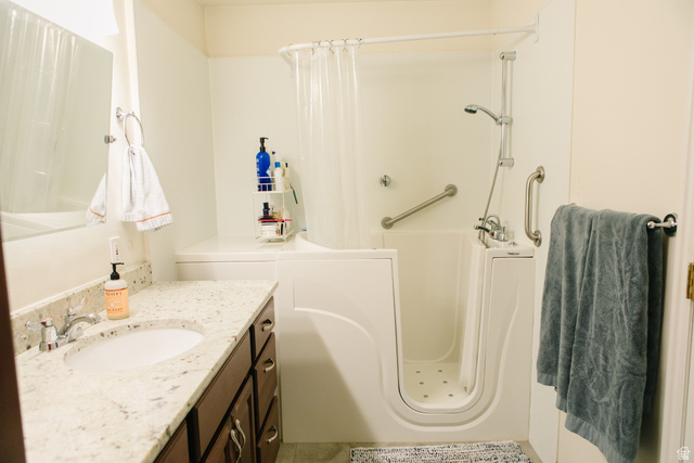 104 South Ridgeview Drive Orem, UT 84058 - Photo 24 of 49 Bathroom featuring a walk-in tub with grab bars, a shower wand, a vanity with a white countertop and integrated sink, and dark wood cabinetry with silver hardware
