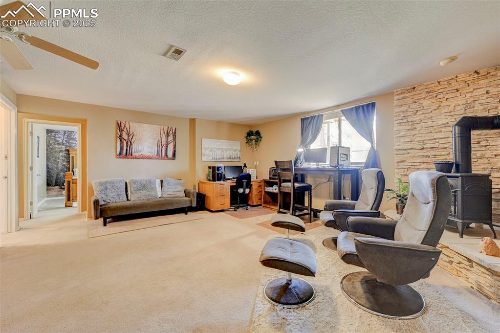 840 West Kelly Road Woodland Park, CO 80863 - Photo 25 of 47 Carpeted living area with a ceiling fan, visible vents, a textured ceiling, and a wood stove