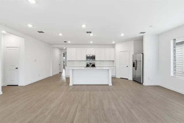 a view of kitchen with stainless steel appliances kitchen island wooden floors and white walls