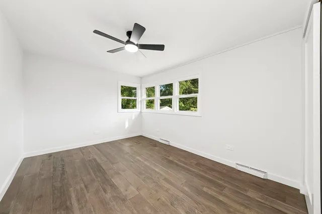 an empty room with wooden floor ceiling fan and windows