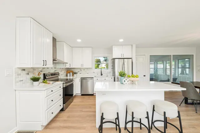 a kitchen with stainless steel appliances kitchen island granite countertop a stove a refrigerator a sink a dining table and chairs