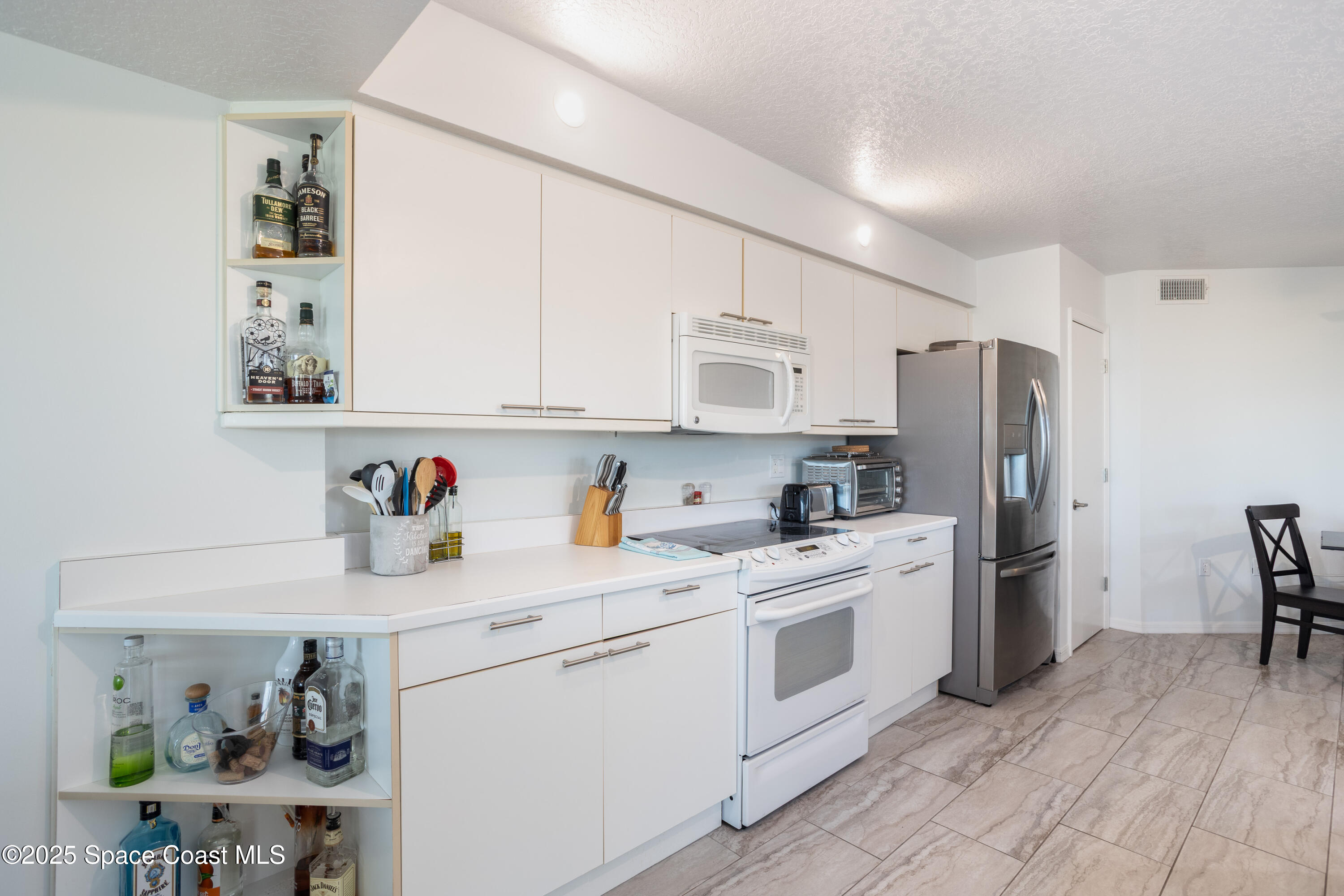 3450 Ocean Beach Boulevard, Unit 201 Cocoa Beach, FL 32931 - Photo 11 of 48 a kitchen with stainless steel appliances white cabinets and a refrigerator