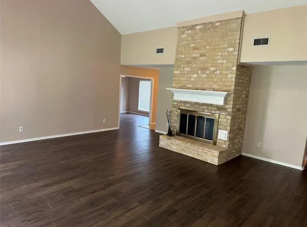 a view of an empty room with wooden floor and a fireplace