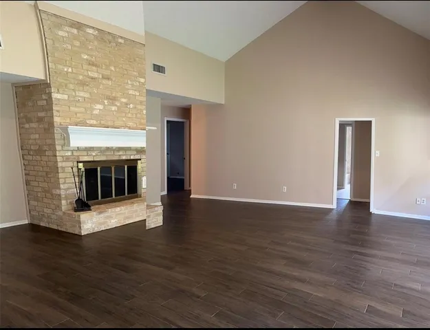 a view of an empty room with wooden floor and a fireplace
