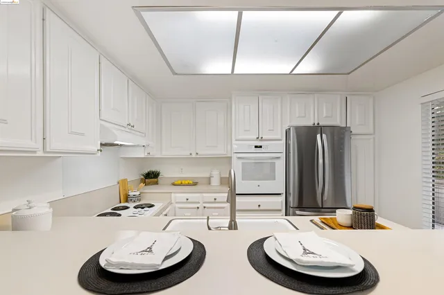 a kitchen with stainless steel appliances a refrigerator a sink a stove a dining table and chairs with wooden floor