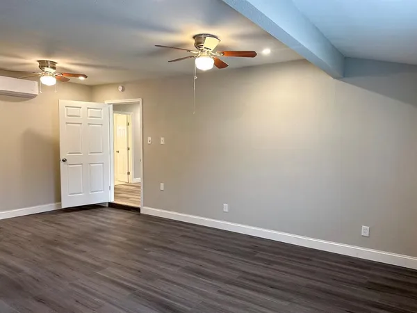 a view of an empty room with wooden floor and a ceiling fan