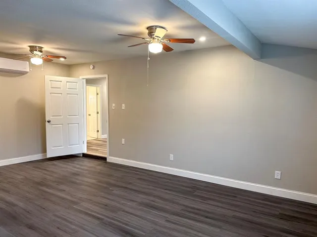 a view of an empty room with wooden floor and a ceiling fan