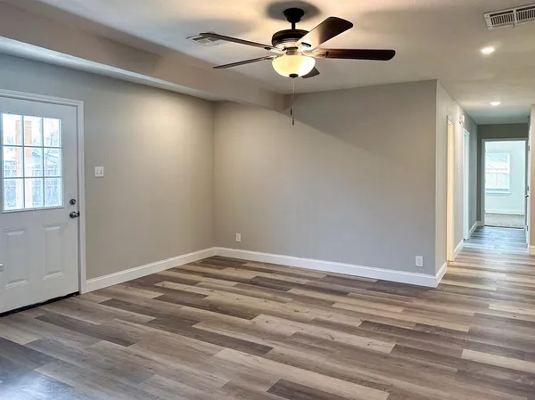 an empty room with wooden floor chandelier fan and windows