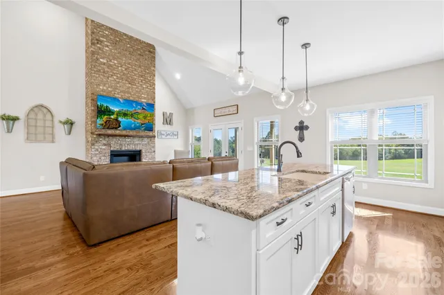 a living room with kitchen island granite countertop wooden floor a large window and a fireplace