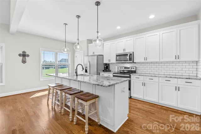 a kitchen with stainless steel appliances granite countertop a stove a sink a microwave a dining table and chairs with wooden floor