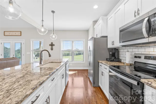 a large kitchen with granite countertop a stove a sink dishwasher a refrigerator and a fireplace with wooden floor