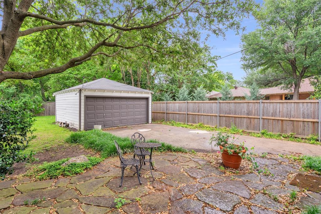 4815 Kelman Street Dallas, TX 75214 - Photo 36 of 37 Detached garage with a paneled garage door, concrete driveway, flagstone patio, wood privacy fence, and mature trees