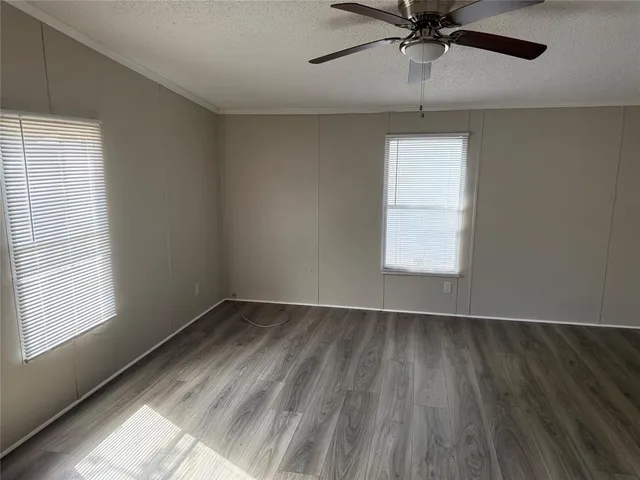 an empty room with wooden floor fan and windows