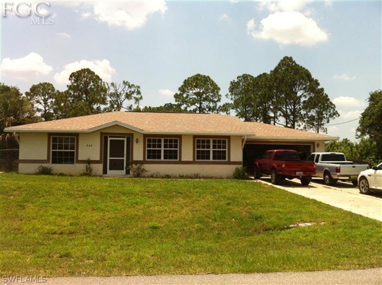 348 Rancho Avenue Lehigh Acres, FL 33974 - Photo 1 of 10 a front view of a house with a garden and trees