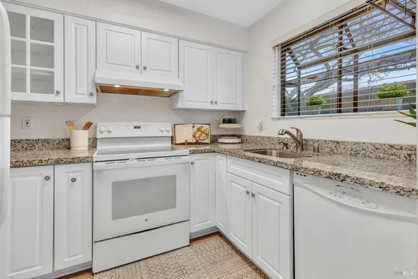 a kitchen with granite countertop white cabinets stainless steel appliances a sink and window